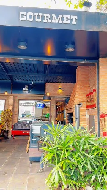 Fachada do HB SteakHouse: toldo azul-marinho com o letreiro GOURMET, paredes de tijolo e balcão na entrada