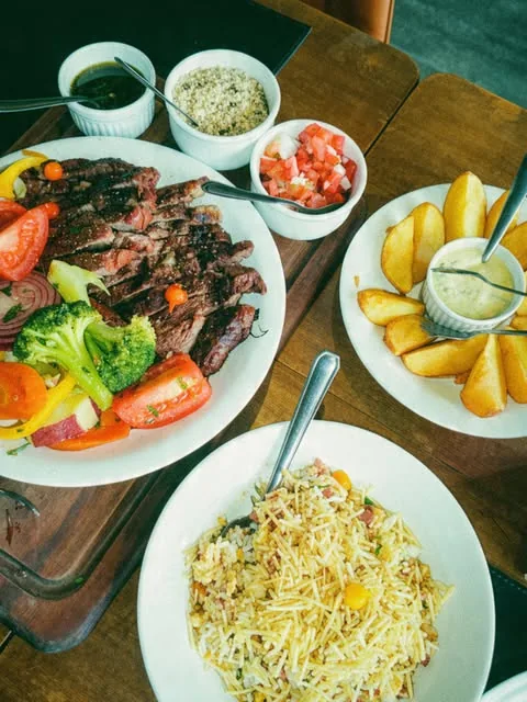 Mesa com carne fatiada, salada, arroz e acompanhamentos