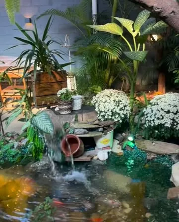 Laguinho com pequena cascata cercado de plantas e flores brancas